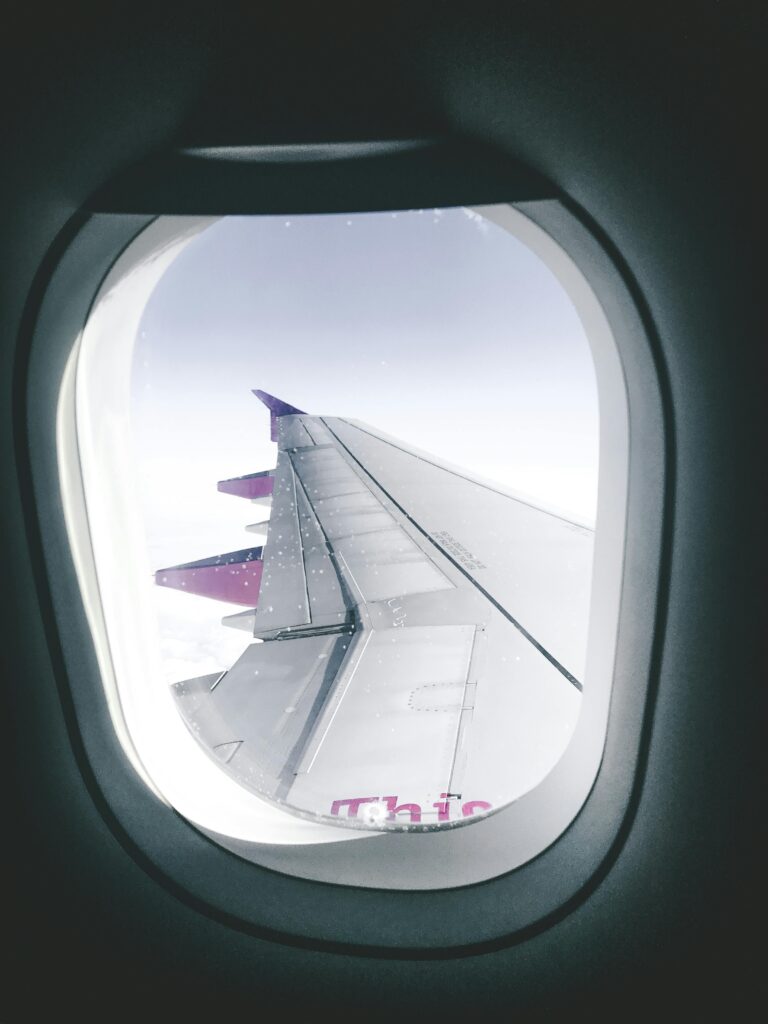 pexels-photo-2364397-2364397 View of an airplane wing through a window, capturing flight over clouds.